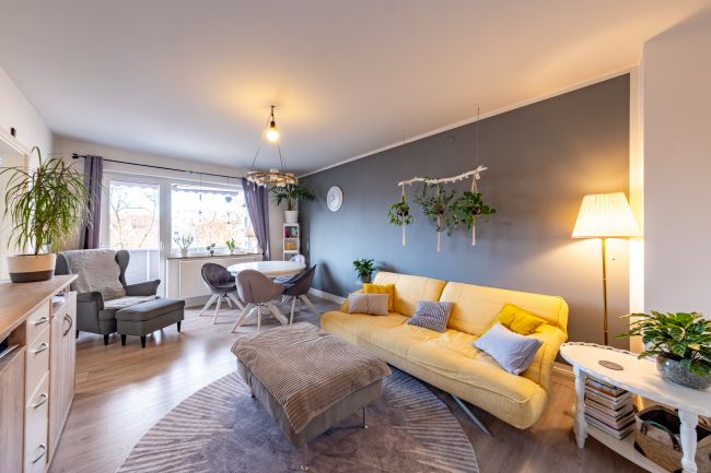 Helles, einladendes Wohnzimmer mit großem Fenster, gemütlichem Essbereich und modernem Wohngefühl.